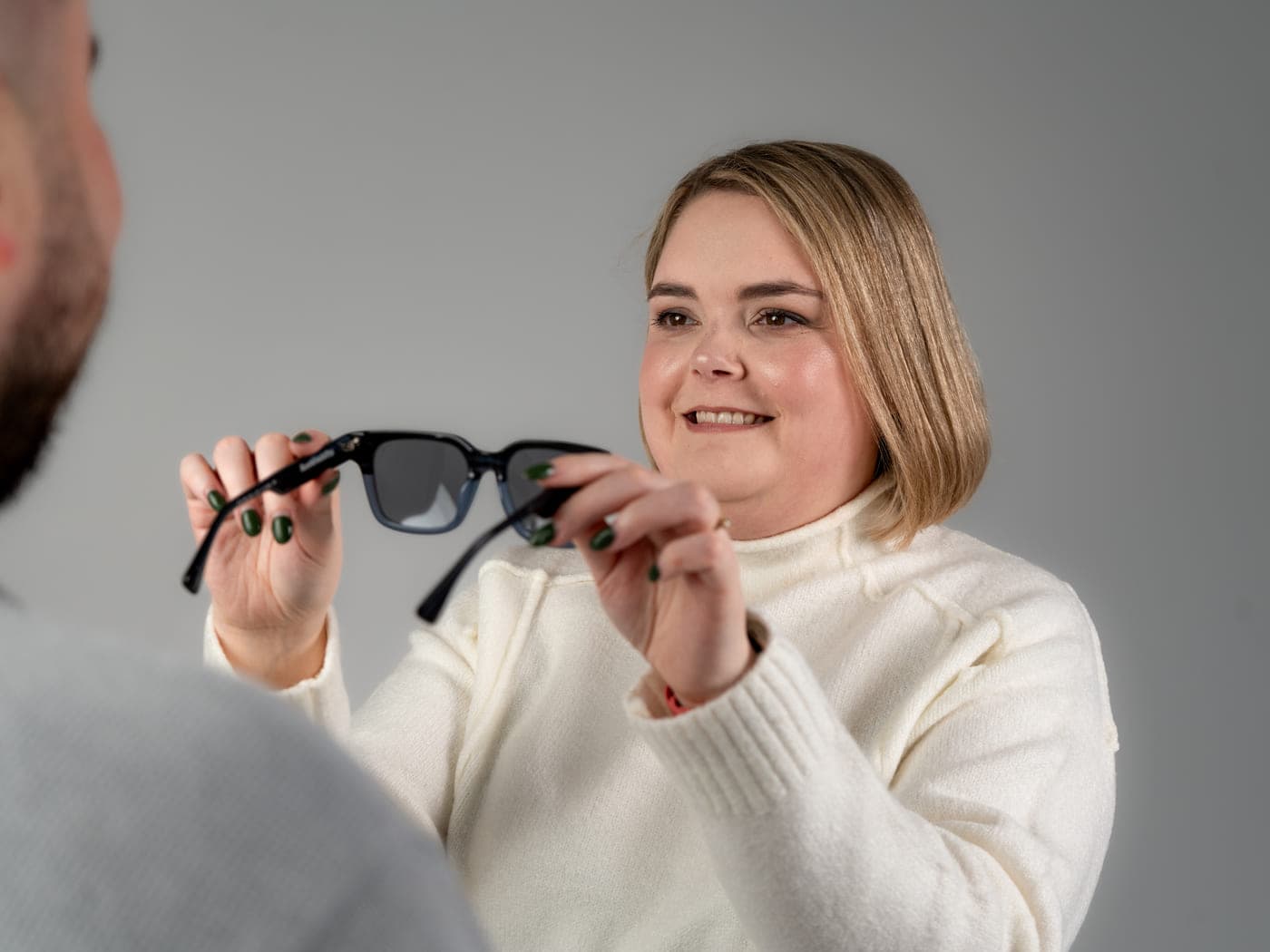 Sabrina tend une paire de lunettes de soleil à un client pendant un essayage.