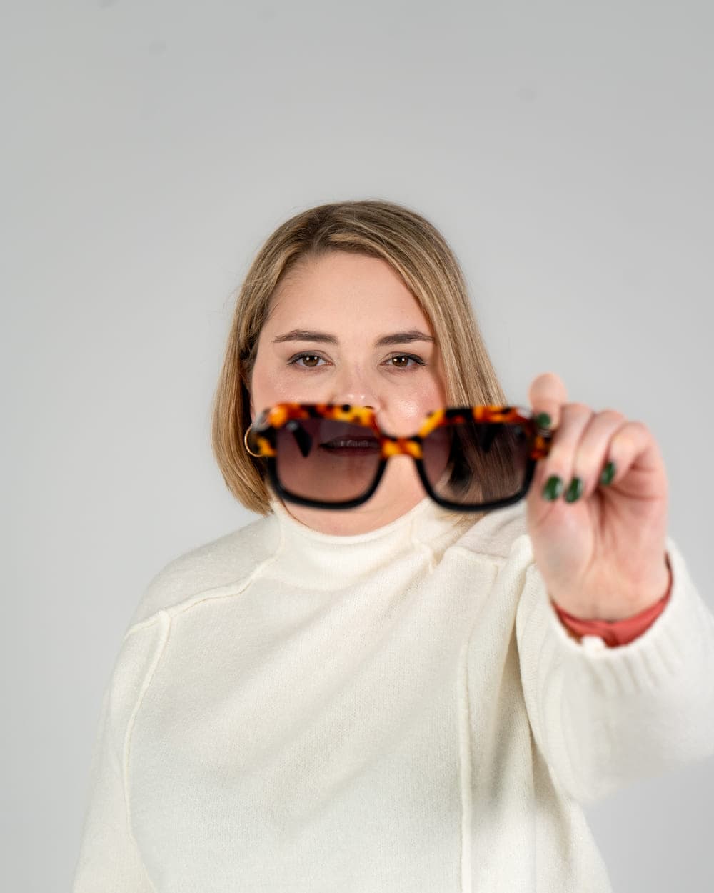 Sabrina holding a pair of tortoiseshell sunglasses up towards the camera, smiling behind them.